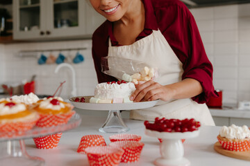 Close-up of joyful female confectioner decorating cake with marshmallow at the kitchen