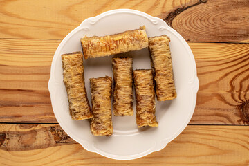 Several pieces of sweet baklava on a white ceramic plate on a wooden table, close-up, top view.