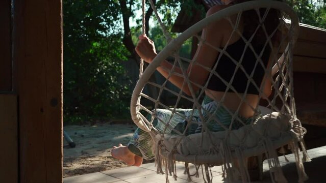 young female riding on macrame swing chair at country house terrace outdoors