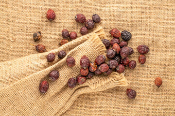 Several dry rose hips with jute bag on jute cloth, macro, top view.