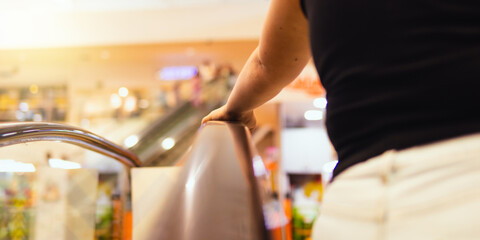 A Latina woman ascends the escalators in a shopping mall. In the foreground, the focus is on her...