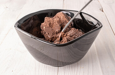 Chocolate ice cream in a ceramic dish with a metal spoon on a wooden table, macro.