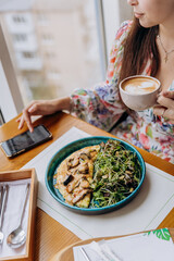 Young beautiful stylish woman drinking coffee while sitting in restaurant and eating tasty dish