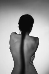 Black&white photo of beauty curves: sensual girl standing back to camera with hands on back with shadow, gray copy space background. Concept of depression, emotion, anxiety, stress, mental health - obrazy, fototapety, plakaty