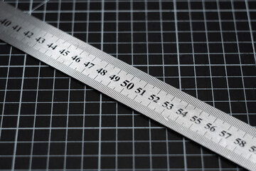 A metal ruler on the mark of 80 centimeters against the background of the grid on the cutting mat.