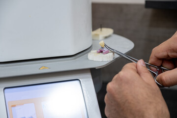 Technician operates high temperature furnace to bake prosthetic ceramic teeth in dental laboratory.