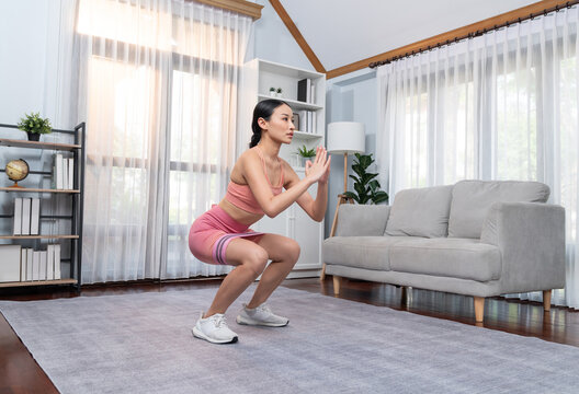 Vigorous energetic woman doing exercise at home. Young athletic asian woman strength and endurance training session as home workout routine with squat.