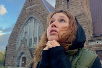 Portrait of young sad praying woman or religious teenager girl on Catholic Church background. 