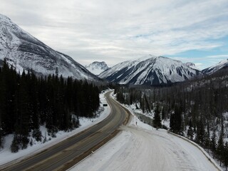 Image of a road during winter with snowcapped mountains in the background and trees along the road
