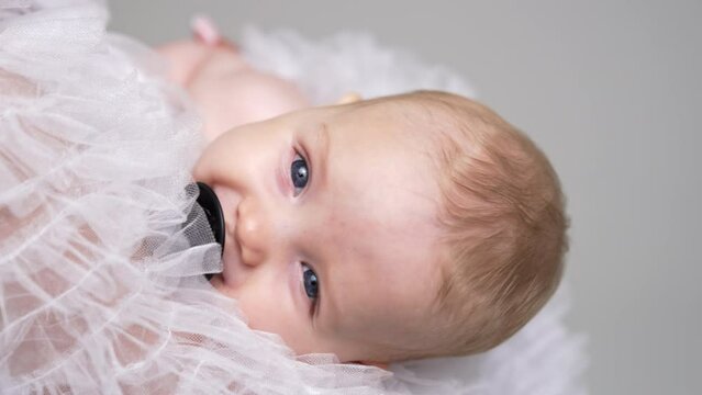 Face of an adorable grey-eyed Caucasian baby with pacifier. Infant swayed in mom's hands falling asleep. Close up.