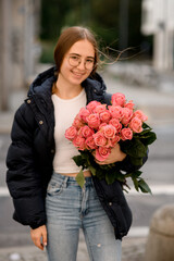 Girl stands on a city street with a bouquet of the pink roses