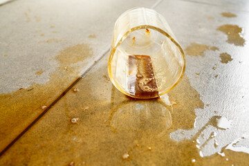 Shot of broken glass cup with poured coffee on tile floor
