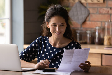 Smiling woman checking financial documents, calculating bills or taxes at home, using laptop and calculator, happy young female planning managing budget, household finances, holding receipt