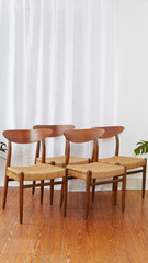 Set of four vintage minimalist cord chairs.  Elegant Mid-Century Modern design. Interior photograph with long white curtains and houseplants.