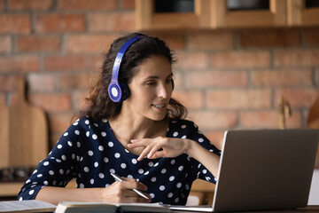 Smiling woman in headphones involved in online course, using laptop, looking at screen, female...