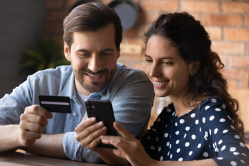 Close up happy young couple making secure internet payment, smiling man and woman using smartphone,...