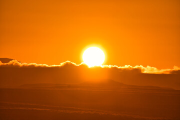 Sonnenaufgang in der Wüste hinter einer Düne über Wolken am Himmel