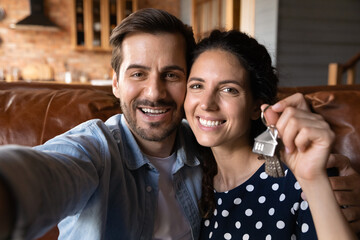 Head shot happy young couple showing keys, hugging, sitting on couch, excited by relocation,...