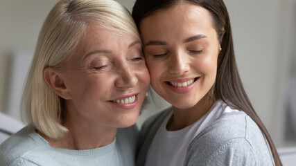 Close up smiling mature mother and daughter enjoying tender moment with closed eyes, happy granddaughter and older grandmother touching cheeks, expressing love and care, two generations bonding