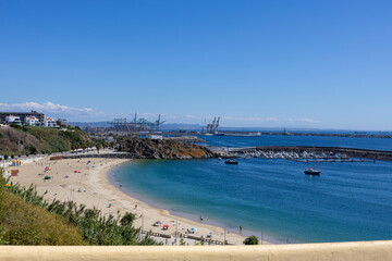 Fototapeta na wymiar View to sines beach with industrial container port terminal cranes behind, in the city of Sines on the South of Portugal