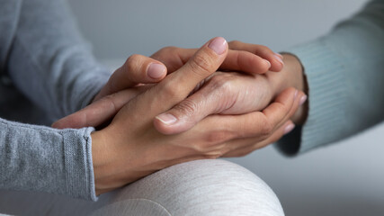Close up young daughter comforting mature mother, granddaughter holding older grandmother hand,...