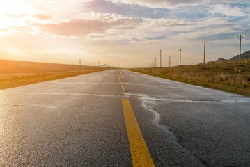 Beautiful shot of a road between fields under a cloudy sky during a sunset © Wirestock