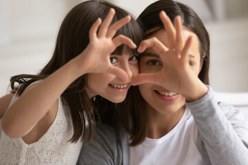 Portrait close up happy mother and daughter showing heart sign with fingers, looking at camera,...