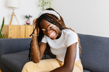 Joyful young african woman laughing sitting on sofa at home. Happiness, diversity and people concept. - obrazy, fototapety, plakaty