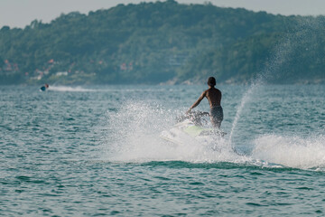 Very well fit man drive jet ski from shore to open sea, splashing water. Tropical beach resort.