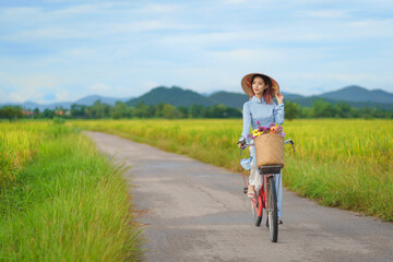 Beautiful Vietnamese Asian woman wearing a blue color Ao Dai National Costume Dress with red bicycle and flowers fresh yellow rice fields mountain background. Portrait fashion show in nature.