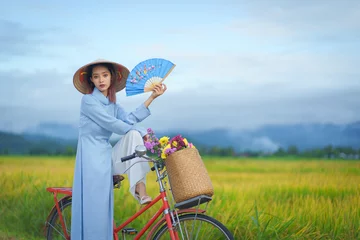 Papier Peint photo Mu Cang Chai Beautiful Vietnamese Asian woman wearing a blue color Ao Dai National Costume Dress with red bicycle and flowers fresh yellow rice fields mountain background. Portrait fashion show in nature.