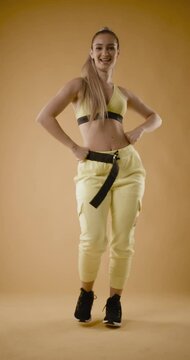 Beautiful girl in yellow outfit dancing zumba. Happy dance instructor against dark yellow background. Vertical video.