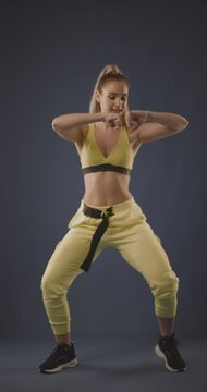 Beautiful blond girl in black outfit dancing zumba against dark blue background. Vertical video.
