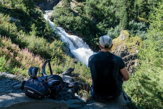 Hiker with backpack on the top of the mountain looks at the Rutor waterfall, Aosta Valley