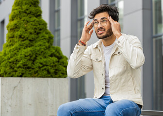 Displeased sick ill Indian man rubbing temples to cure headache problem, suffering from tension...