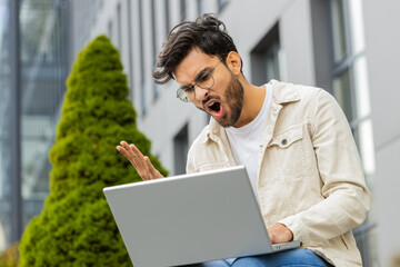 Displeased Indian man use laptop typing browsing working, loses becoming surprised sudden lottery...