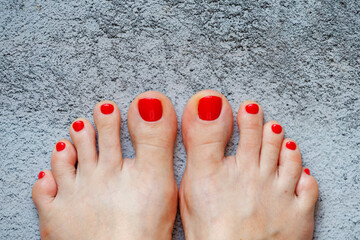 Beautiful woman's red nails with beautiful pedicure. Female feet with bright pedicure on grey concrete background. Autumn and summer concept. Top view, copy space, horizontal, close up