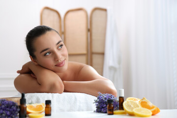 Obraz na płótnie Canvas Beautiful young woman relaxing on massage couch and bottles of essential oil with ingredients on table in spa salon