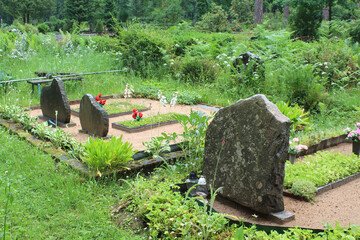 Three gray headstones in a cemetery with flowers in Ogre, Latvia