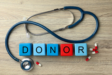 Word Donor made of cubes, stethoscope and pills on wooden table, flat lay