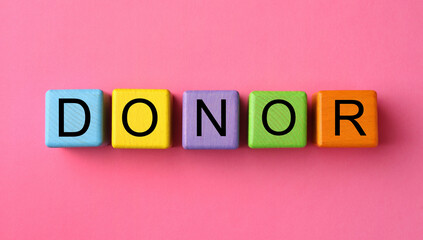 Word Donor made of colorful wooden cubes on pink background, flat lay