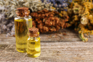 Bottles of essential oils and many different dry herbs on wooden table, closeup. Space for text