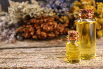 Bottles of essential oils and many different dry herbs on wooden table, closeup. Space for text