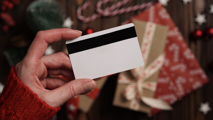 Hands of a woman in a red sweater with a credit card on a background of gift boxes, selective...