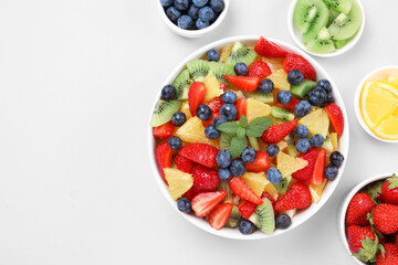 Yummy fruit salad in bowl and ingredients on light background, flat lay. Space for text