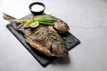 Seafood. Delicious baked fish served with green onion and lime on light textured table, space for text