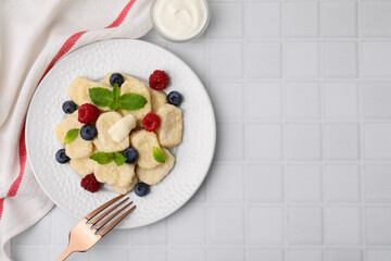 Plate of tasty lazy dumplings with berries, butter and mint leaves on white tiled table, flat lay. Space for text