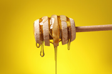 Delicious honey flowing down from dipper against yellow background, closeup