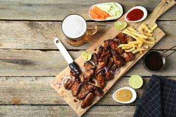 Tasty roasted chicken wings served with beer on wooden table, flat lay. Space for text