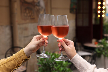 Women clinking glasses with rose wine outdoors, closeup